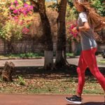 A woman jogs on a path surrounded by trees and vibrant flowers, embodying a healthy lifestyle.